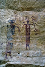 And here we have a closer look. There appears to be some spalling that has destroyed some of the detail. Both figures have associated snakes but only the right figure is touching the snake. The snake is near but below head level of both figures. there are four hollow circles to the right of the right figure. There does not appear to be any  corresponding feature to the left of the left figure. I try to pay attention to symmetry or lack thereof. The figure at the left has open or loop feet, the figure at the right has solid feed. Both share the same proportion of body to legs, arms and head. The figure at the left has two concentric circle eyes while the figure at the right has a distinctly smaller head and no eyes. The figure at the right has a circular decoration on the chest that appears to consist of three concentric circles as opposed to a spiral. To the left of the left figure there are some smudges and spall areas that indicate something was here originally.  Would it have provided symetry?? Unfortunately they cannot be recovered with visible light photography. And yes, the figures are two distinct colors, but portions of each appear in both colors.  Significant???