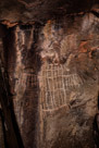 This Dinwoody character has a lot of symetry yet some very distinct unsymetrical  elements. There are three 'antanae'  to the left and three to the right. The 'wings' each have seven 'feathers' and there are three left 'toes' and three right. The torso is divided into six vertical columns by five bold vertical lines. However, the bold horizontal lines to not appear to go all the way across in some cases and the thin horizontal lines certainly do not and appear to be placed indifferently. The figure has been highlighted with chalk and appears to have suffered a couple of gun shots to the head. There appear to be some 'whisker' type lines on the remains of the head.