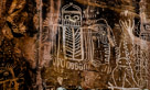 This is the first figure on the main panel. I think.  I will discuss only the center figure here. I cropped the original picture wide so it will display the caption better on most browsers. In any case I have isolated this portion of the rock art and declared it a figure but all the figures are more or less connected so that will be addressed in a later image.  
I would like to have a frank exchange of ideas with the person that chalked this in.  
This is and owl like Dinwoody figure but it has stubby arms and five fingered hands indicated right and left. Neither legs nor feet are indicated but four 'toes' are indicated at each lower corner of the torso. Two bold eyes without pupils are indicated in the head. The number eight is indicated in several ways on this figure. There are eight vertical lines in the 'mouth' under the eyes. (don't do by the chalk).  There are eight bold vertical bars to the left and right of the head. A second row of vertical bars may also have eight members on each side but other features were pecked over them probably in the original creation. There are also eight ovals under the figure. Note the three lines descending from the three left ovals. Significant??? The head appears to have 'whiskers' under the 'mouth'  indicated by ten short vertical lines.  The torso is divided down the middle with uprising horizontal lines, eight to the right and ten to the  left.  To the left there is a wavy jagged line descending from the left bottom finger.  On the right there is a much more complex relationship with the adjacent figures. From the top, there appears to be a line emitted from the right shoulder becoming wavy and dropping to the figure(s) below.  Then the right hand appears to hold a 'comb' and the top two fingers emit a line or lines to a figure below. From the lower fingers/comb are two loops and a line with five loops attached. And the figure has paired inward pointing horns.  Just visible to the lower left is a similar figure, much simplified with a five fingered hand raised. A warm-up for the main figure???