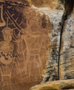 Another one of the 'Three' kinds. 
But first we must separate this king from an underlying petroglyph of possibly another older kind. 
If you look closely there is a fully pecked character underneath with a tringular body and fully pecked feet indicated both left and right. The 'horns' eminating to the left are probably part of the head treatment for this old 'king'. 
Our king appears to be wearing a mask with a very elaborate headdress. Feathers (antlers?) are indicated a part of this headdress. There appear to be two eye slots in the mask. Two square ear rings hang below the mask. A large brestplate is indicated. The trapazoid body is emphasized with very heavy  full pecking possibly to distinguish this glyph from the underlying glyph.  There is some indication that this king was painted at some point. The right foot appears to be decorated?.  A broad but relatively plain belt is indicated. The left arm if it ever existed is lost to spalling. No weapon is indicated.